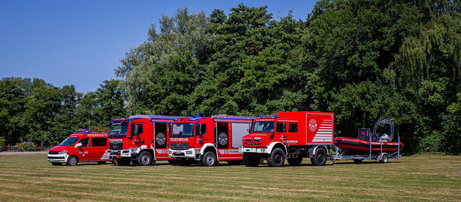 Der Fuhrpark der Freiwilligen Feuerwehr Ostseebad Dierhagen in einer Reihe auf einer Wiese: ELW 1, HLF 20, LF 20, Gerätewagen Wassergefahren und das Rettungsboot auf dem Trailer